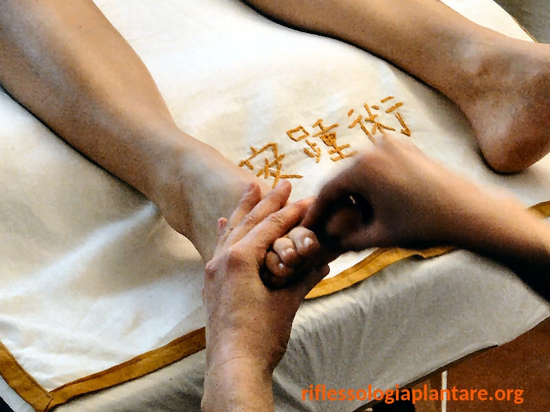 Due mani che eseguono un trattamento di riflessologia plantare On Zon Su® su un piede, con ricamo del nome in caratteri cinesi sul lenzuolo, in sintonia con l'antica tradizione asiatica del metodo.